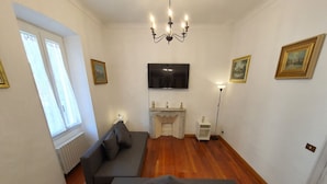 Una sala de estar con un sofá gris, una chimenea, un televisor de pantalla plana y una araña.