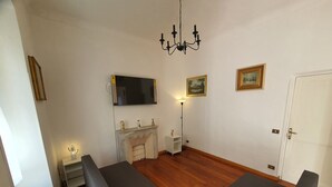 Una habitación con dos sofás grises, un televisor de pantalla plana, una chimenea blanca y una araña.