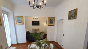Un comedor con una mesa de vidrio dispuesta para seis personas, rodeado de sillas blancas. Un candelabro cuelga del techo y hay obras de arte enmarcadas en las paredes.
