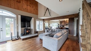 A spacious living room with a large gray sectional sofa, a fireplace, wooden floors, and a lofted ceiling.