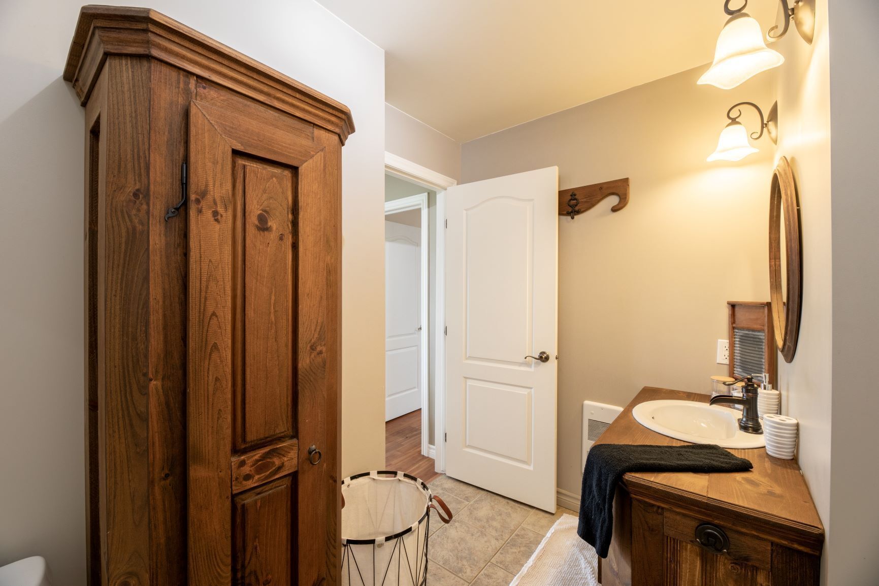 Une armoire en bois, une porte blanche, une salle de bain avec un lavabo et un miroir, et un luminaire.