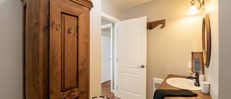 Une armoire en bois, une porte blanche, une salle de bain avec un lavabo et un miroir, et un luminaire.
