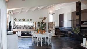A spacious kitchen with a dining area, featuring a stone fireplace, white cabinetry, and a large window. - Villa Cava with private pool (Avola)