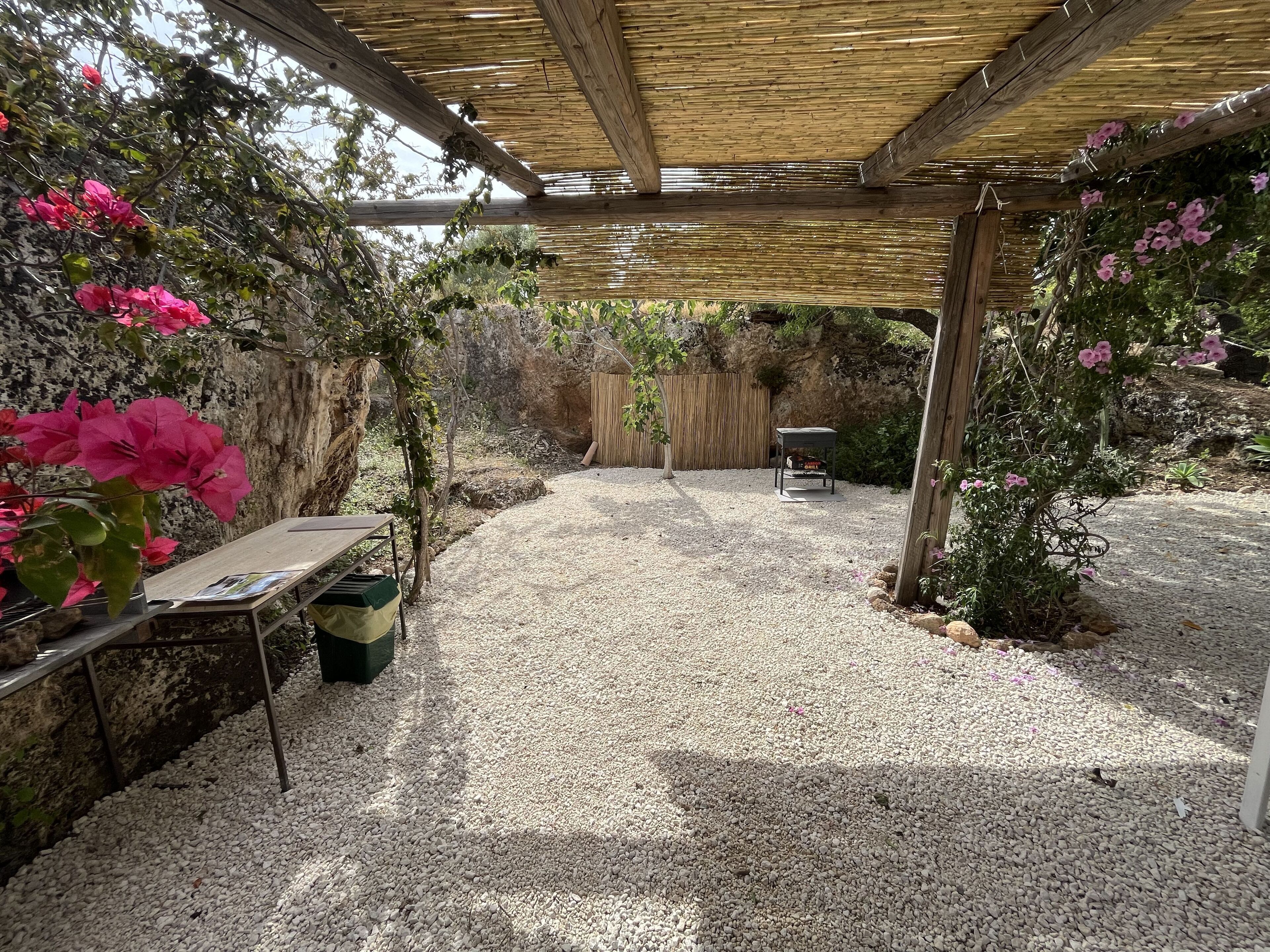 Un espace extérieur abrité, doté d’un sol en gravier, d’une table avec une chaise et d’une structure en forme de pergola.