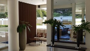 Un hall d’entrée moderne avec un espace salon, de grandes plantes en pot et un mur réfléchissant.