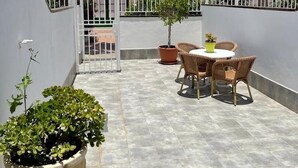 Un patio en la azotea con una mesa y sillas, rodeado de plantas en macetas y una cerca blanca.
