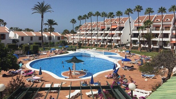 Un hotel con piscina rodeada de tumbonas y palmeras.