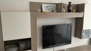 Una sala moderna con un televisor de pantalla plana montado en un mueble de madera, acompañado de un estante inferior con objetos decorativos y un cuenco de vidrio.
