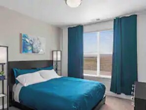 Relax in a spacious room with a large bed, a desk for work, and a window with curtains.