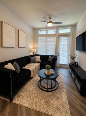 A living room with a black sofa, a round coffee table, and a ceiling fan. - Luxury Modern Apartment In Atlanta wFree Parking  (Atlanta)