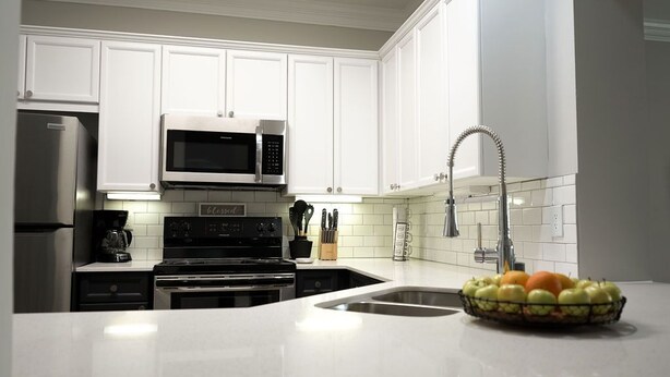 Una cocina moderna con armarios blancos, un refrigerador de acero inoxidable, un microondas y un lavamanos con grifo.