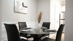 Un comedor con mesa de vidrio, sillas negras y un jarrón con plantas secas.