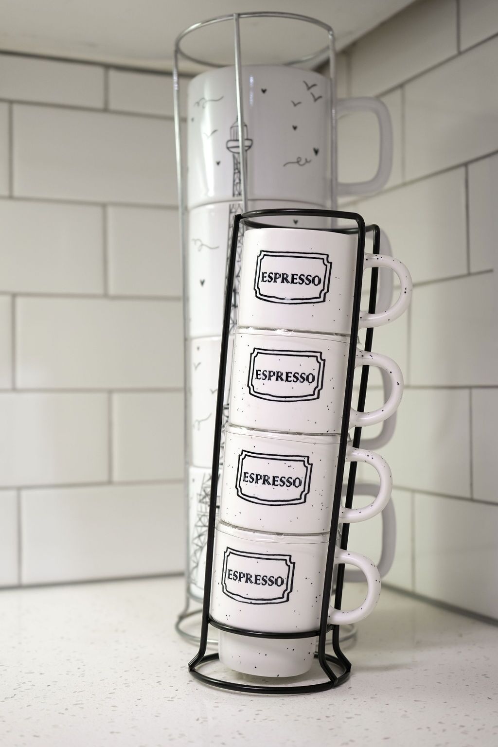 Ein weißer Tassenhalter mit vier weißen Tassen, jede beschriftet mit 'ESPRESSO', vor einer weißen, gefliesten Wand.