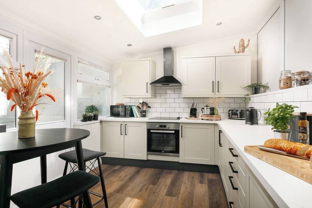 Une cuisine moderne avec des meubles blancs, une cuisinière noire et un puits de lumière.