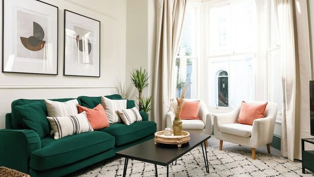 A living room with a green sofa, white armchair, and a coffee table. There are two framed abstract paintings on the wall and a window with curtains. - Luxury for 2024, Central Plymouth Home for 10 (Plymouth)