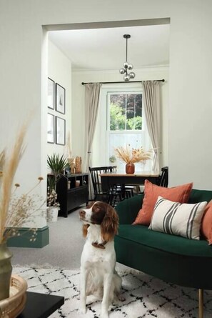 Un salon avec un canapé vert, une table à manger avec des chaises et un chien assis sur le sol.