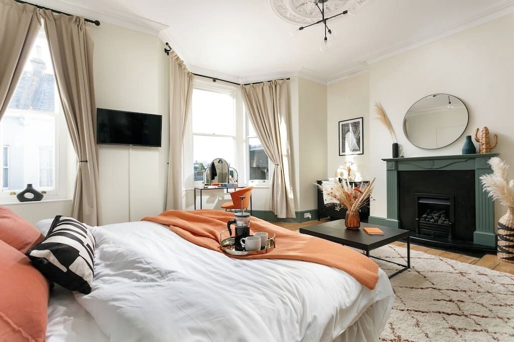 A bedroom with a bed, a coffee table with a tray, a fireplace, and a television on the wall.