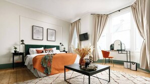 A bedroom with a bed, a bedside table, a TV, a chair, a desk, and a window with curtains. - Luxury for 2024, Central Plymouth Home for 10 (Plymouth)