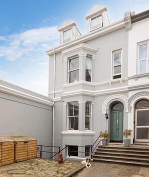 A two-story building with a green door, white trim, and a small front garden with steps leading to the entrance.