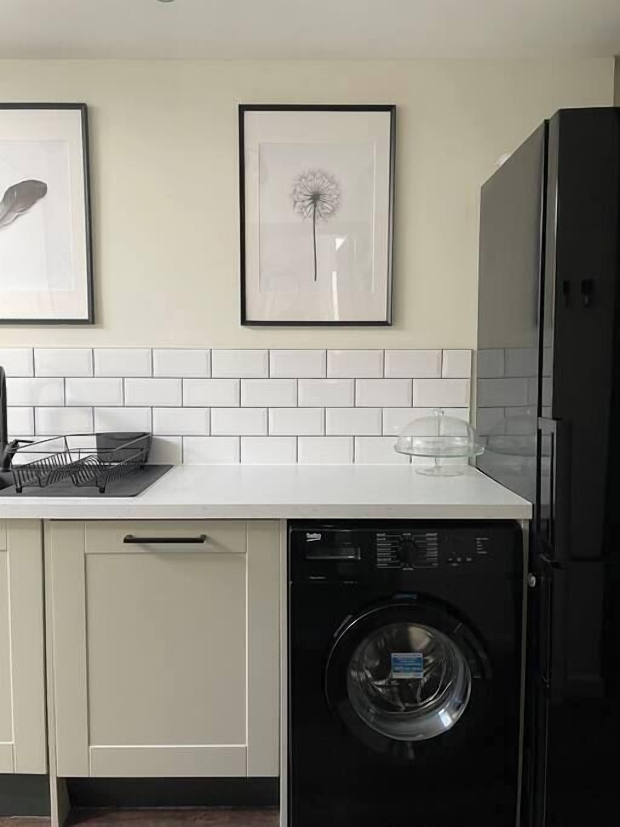 A kitchen with a dishwasher, a sink, and a countertop. There are framed pictures on the wall above the countertop.