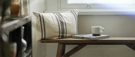 A small wooden table with a white mug and a striped pillow, positioned near a window.