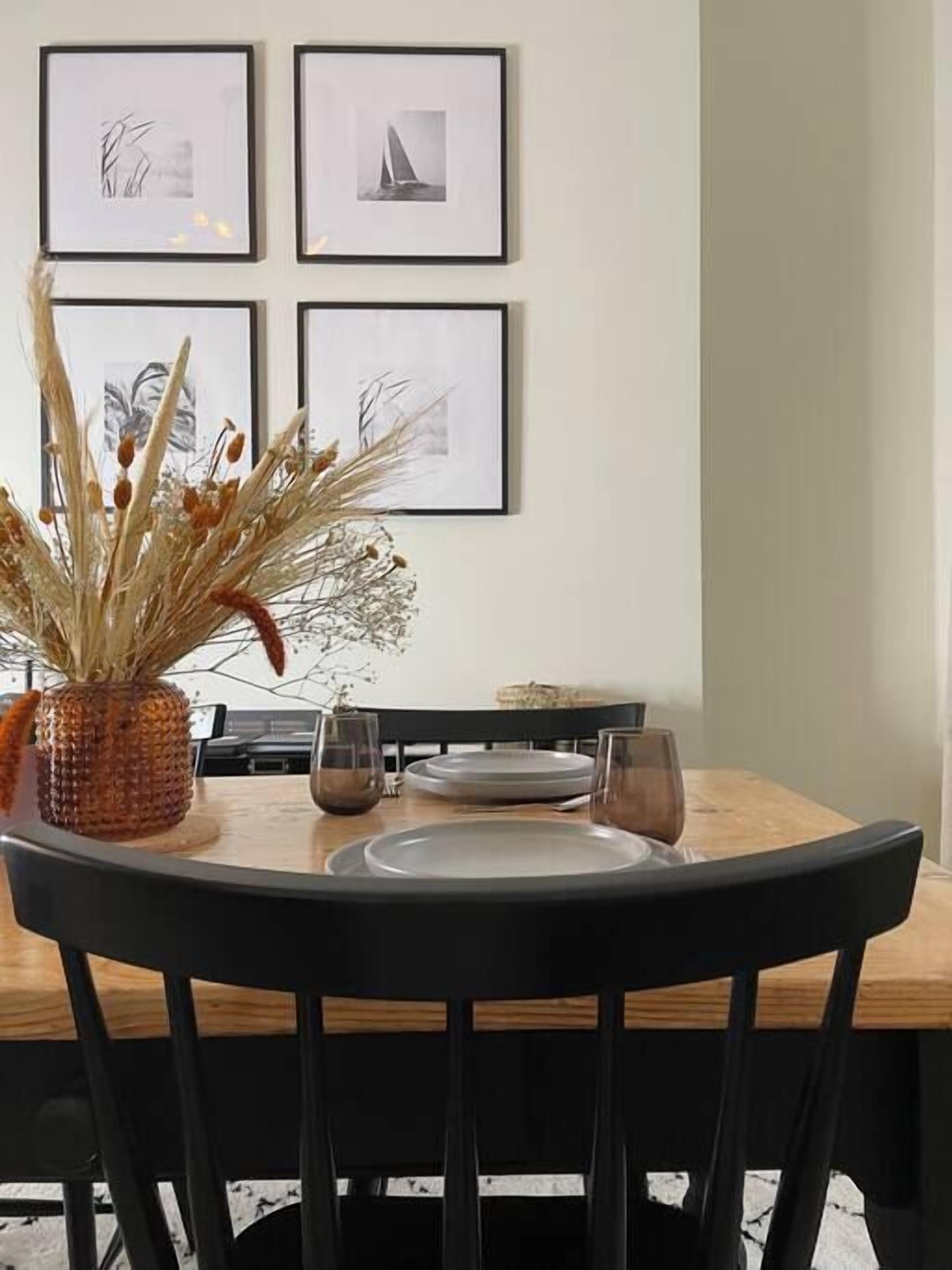 A dining area with a wooden table, black chairs, and framed artwork on the wall.