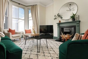 Un salon avec une cheminée, un téléviseur et des canapés verts.