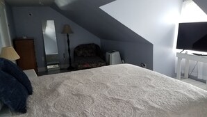 Ein Schlafzimmer mit einem großen Bett, einem Schreibtisch mit Computer, einem Deckenventilator und einem Fenster.