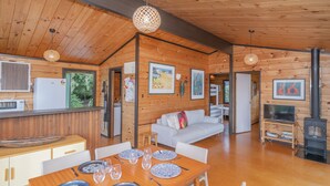 Interior de una cabaña de madera con comedor, sofá, kitchenette y chimenea.