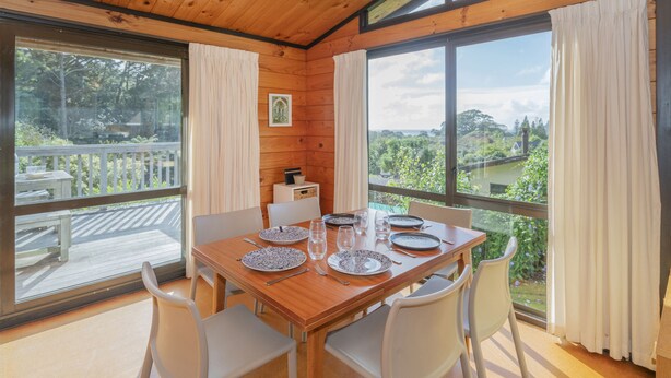 Comedor con mesa de madera para cuatro, ventanas grandes con cortinas y vista a zonas verdes.