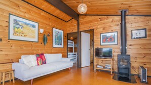 Un interior de cabaña acogedor con un sofá blanco, paredes de madera, una chimenea y cuadros enmarcados.