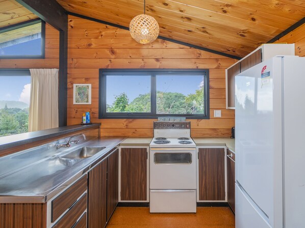 Una cocina compacta con paredes de madera, un ventanal grande, una estufa y un refrigerador.