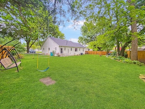 A backyard with a swing set, a house, and a wooden fence.