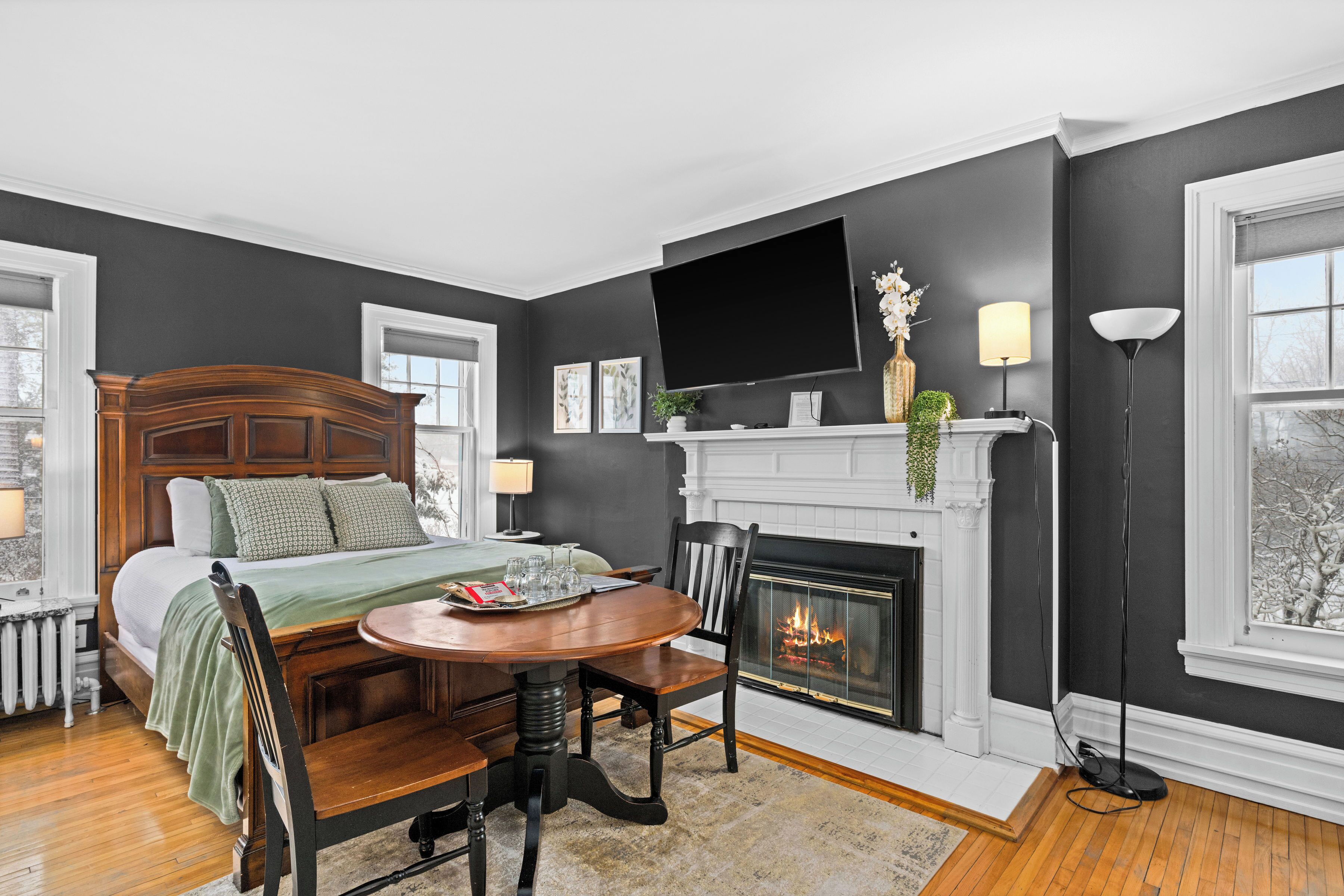 A bedroom with a bed, a fireplace, a TV mounted on the wall, and a dining table with chairs.