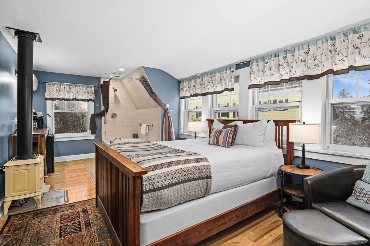 A bedroom with a large bed, a wooden dresser, a radiator, and a window with curtains.