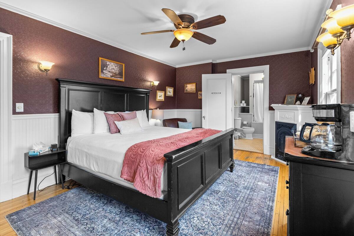 A bedroom with a bed, a ceiling fan, a nightstand, a dresser, and a coffee maker.