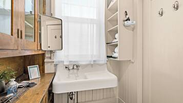 Un baño con tocador de madera, lavamanos blanco, espejo, toallero y zona de ducha.