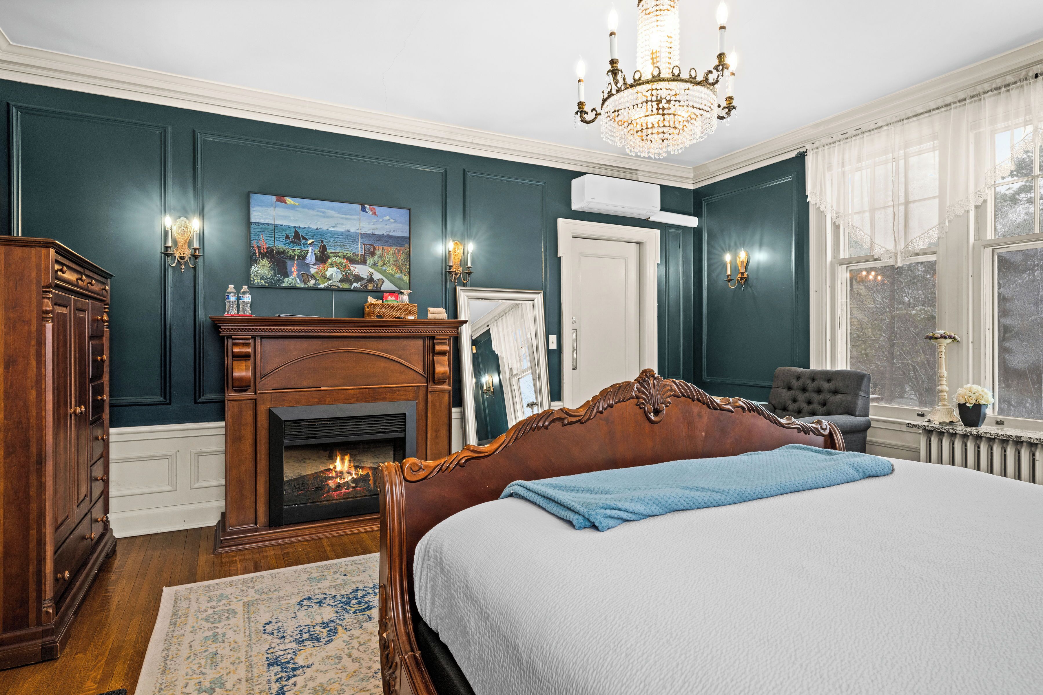Une chambre à coucher avec un grand lit, une cheminée, un lustre et une vue sur l’extérieur par une fenêtre.