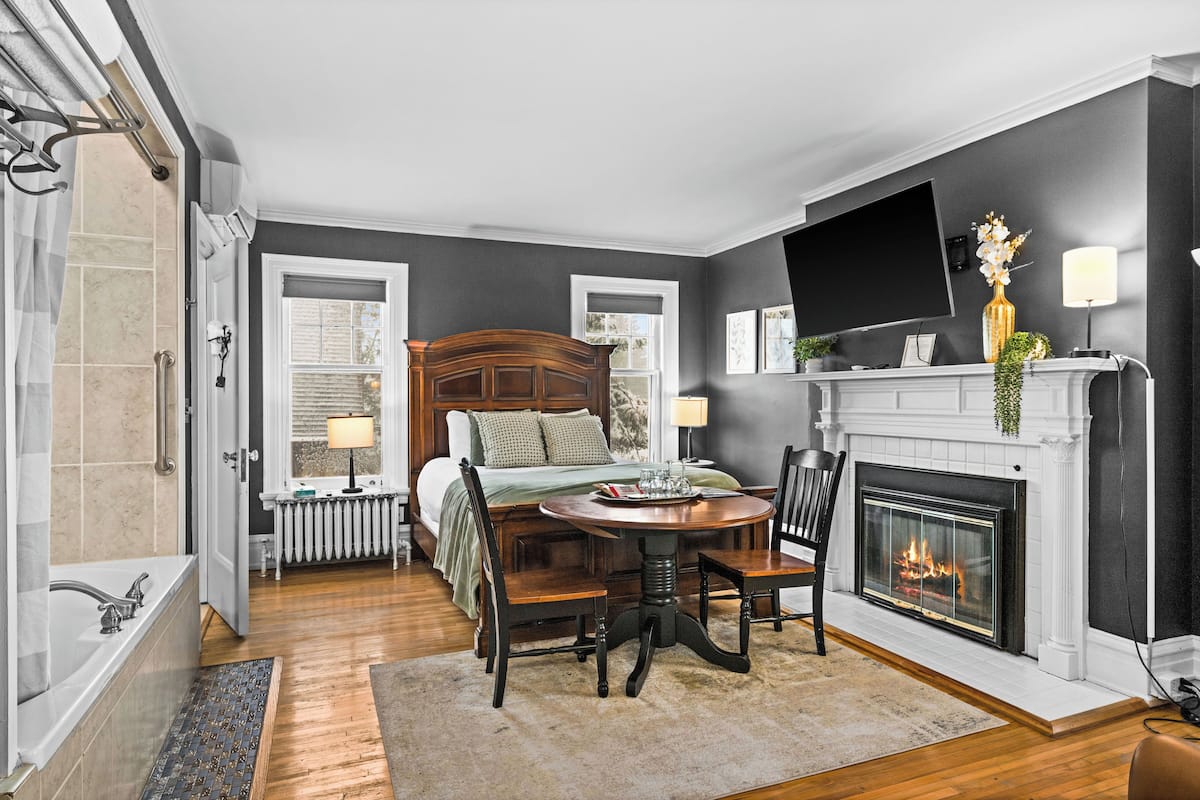 A hotel room with a bed, a fireplace, a TV, and a dining area with a table and chairs.