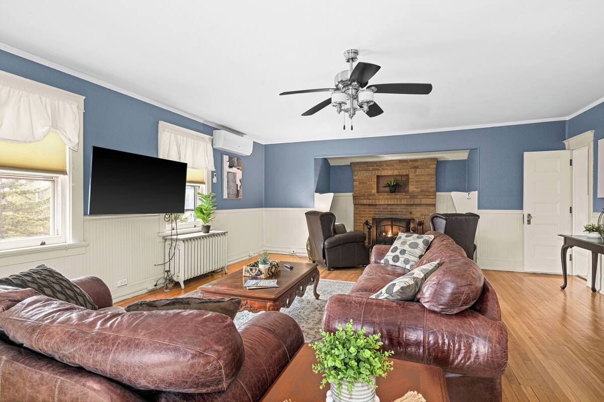 A living room with a fireplace, leather sofas, a ceiling fan, and a television.