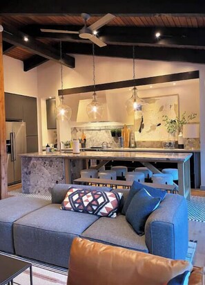 Una cocina moderna con una isla central, una zona de comedor con mesa y sillas, y un rincón de estar acogedor con sofá y cojines.