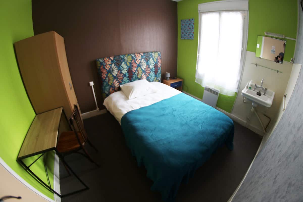 Une chambre à coucher comprenant un lit, une table de chevet, une commode, une fenêtre et une salle de bain avec un lavabo et un miroir.