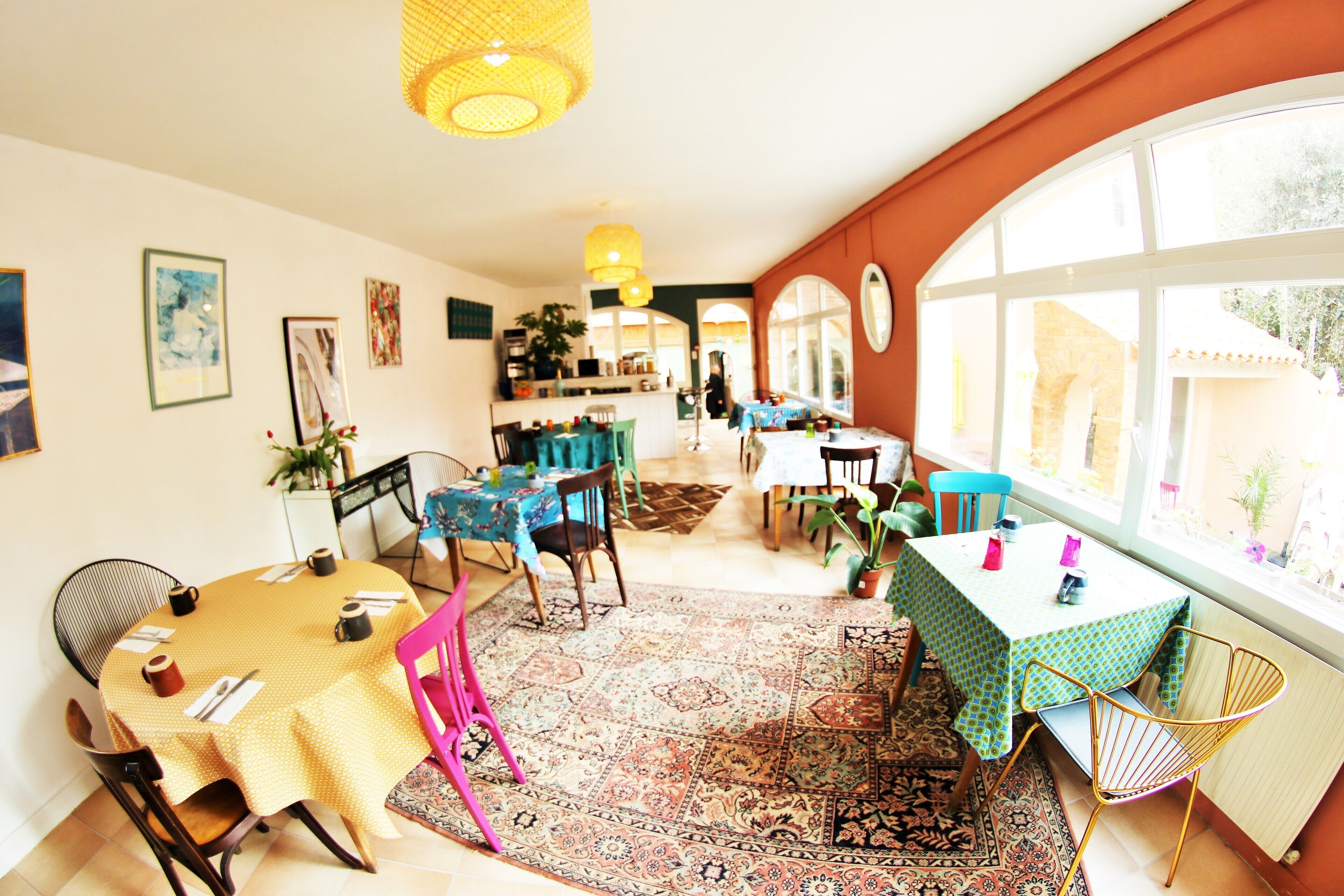 A dining area with multiple tables and chairs, a patterned rug, and large windows with a view of the outside.