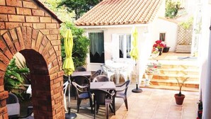 Un espacio al aire libre con paredes de ladrillo, piso de baldosas, mobiliario exterior y plantas en macetas.
