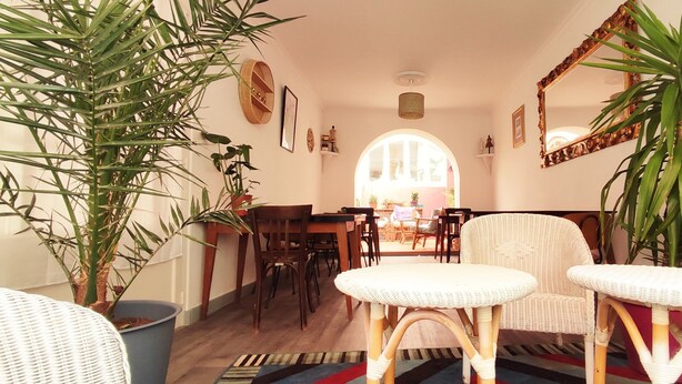 Una sala de estar acogedora con comedor, que incluye muebles de mimbre, plantas en macetas y un espejo grande.
