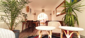 Una sala de estar acogedora con comedor, que incluye muebles de mimbre, plantas en macetas y un espejo grande.