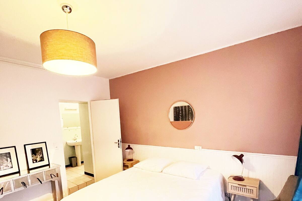 Une chambre d’hôtel avec un grand lit, des tables de chevet, un miroir et une porte donnant sur une salle de bain.