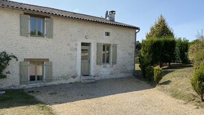 Una casa a due piani con vialetto sterrato e un piccolo giardino.