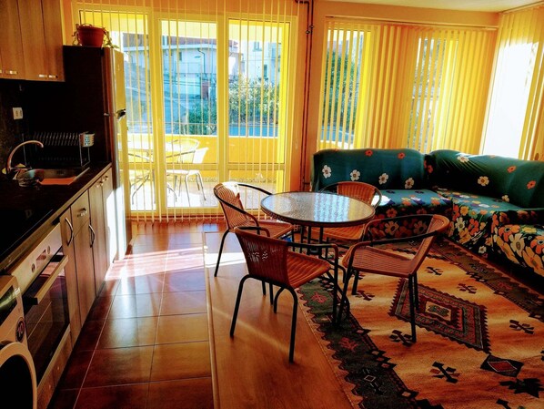 A kitchen with a sink, stove, and cabinets, a dining area with a round table and chairs, and a sofa with a floral pattern.