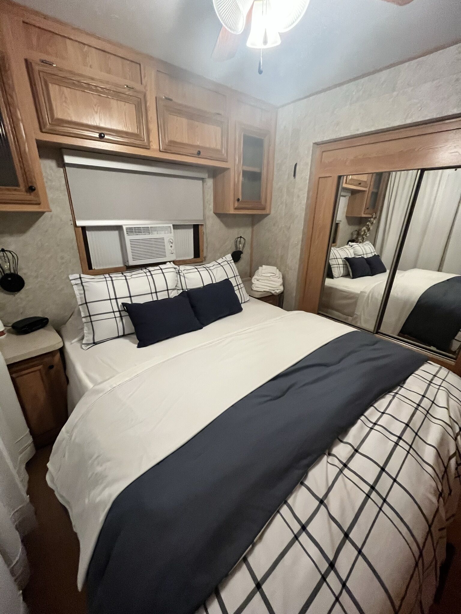 Quarto com cama, armários de madeira, espelho e ventoinha no teto.